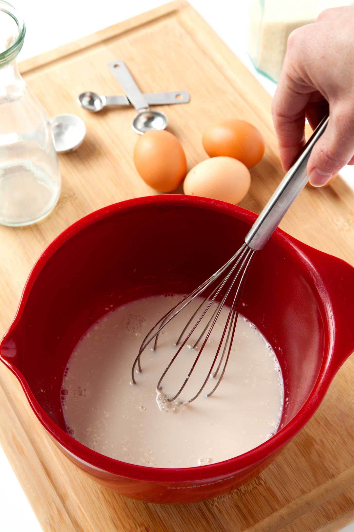 Whisking together french toast batter with eggs and measuring spoons in the background.