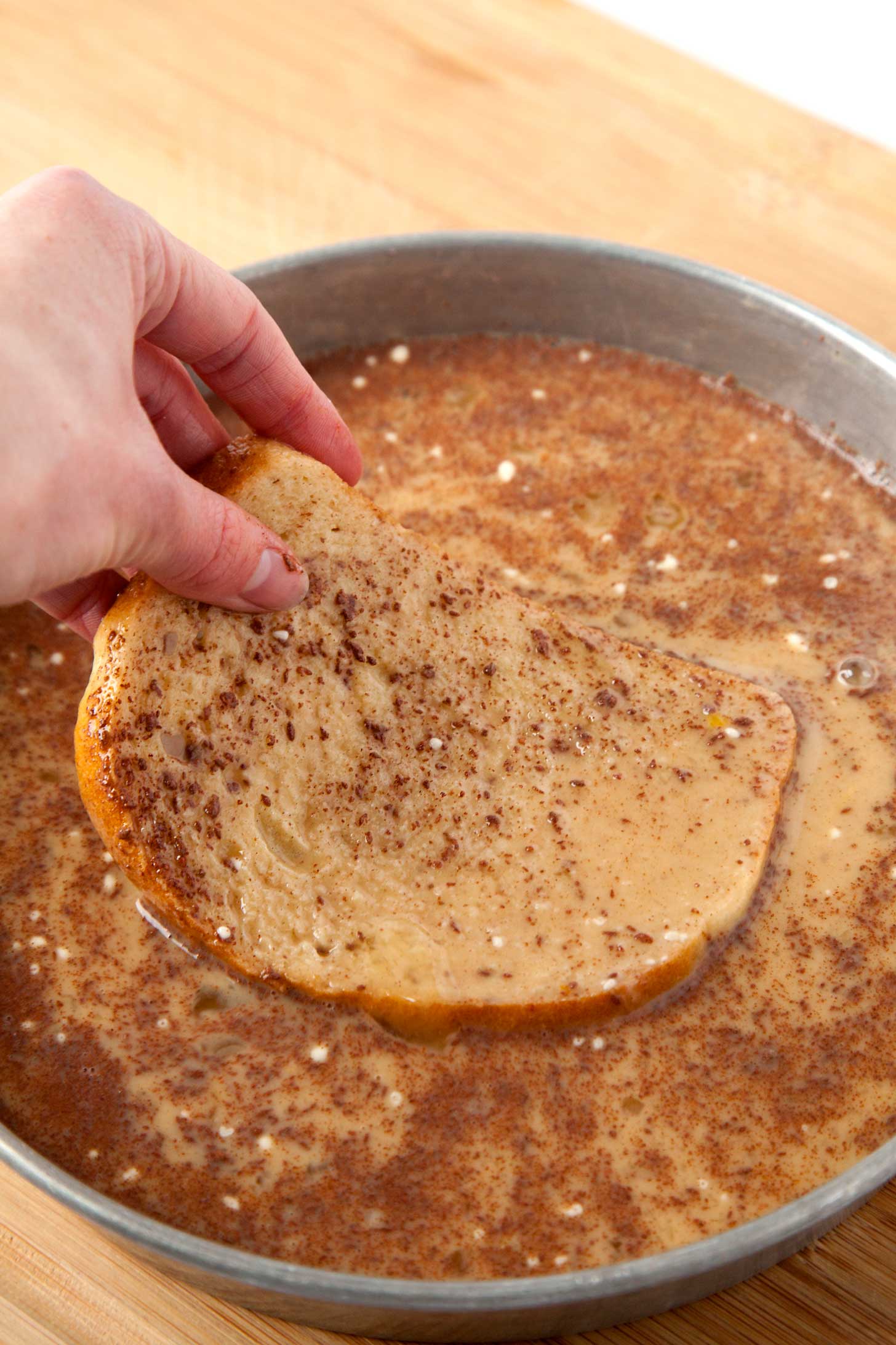 A hand dipping bread into french toast batter.