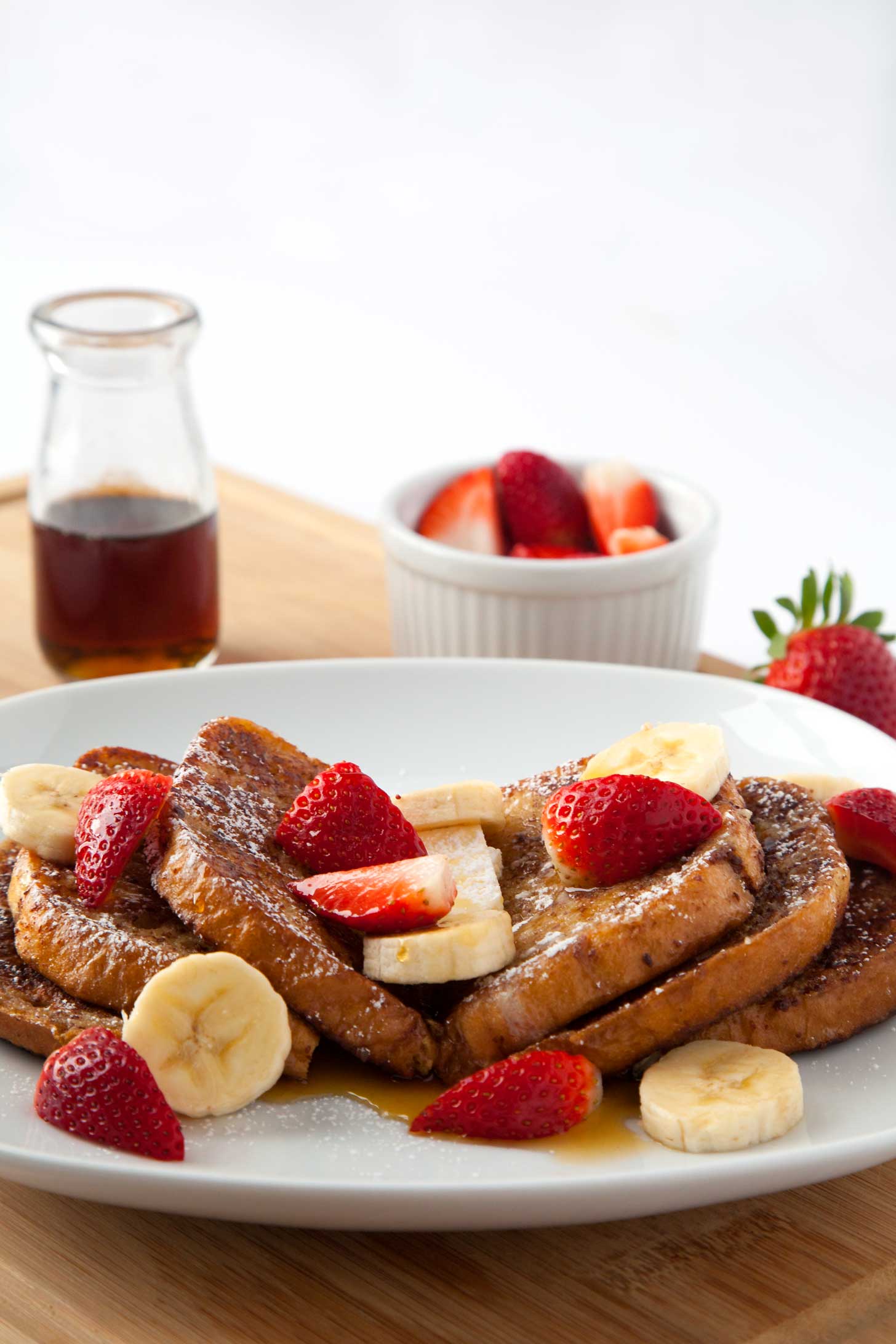 A plate with stacks of french toast, topped with strawberries, bananas, butter, and syrup.