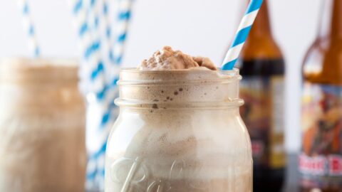 A root beer float with a striped straw, root beer bottles in the background.