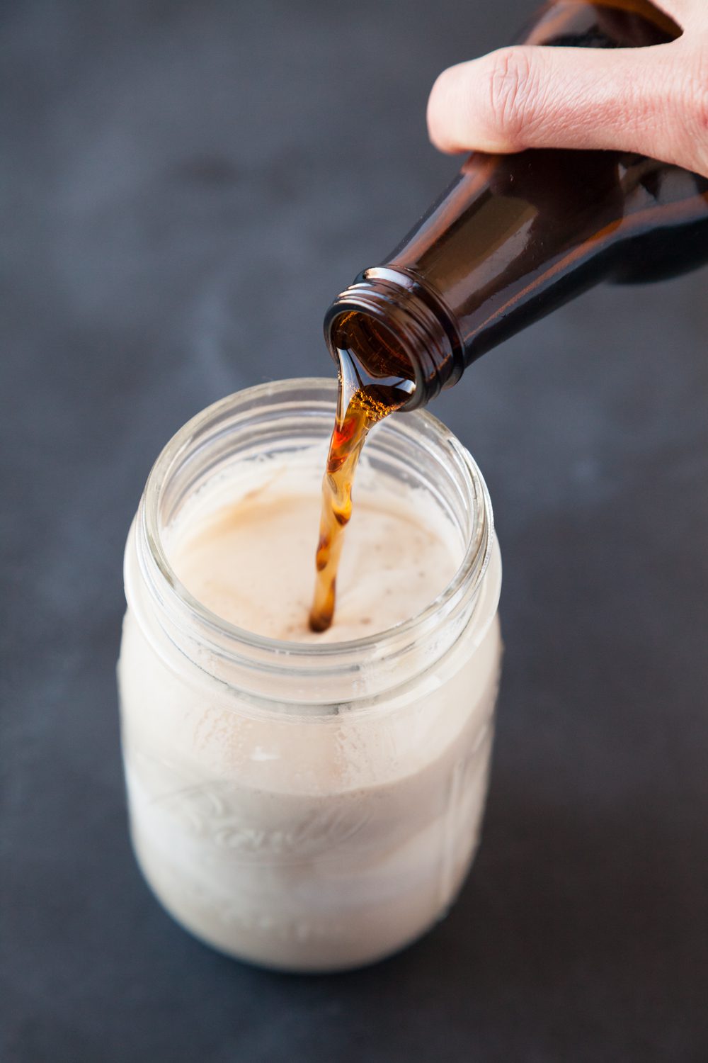 Pouring root beer from a bottle into a glass with ice cream.