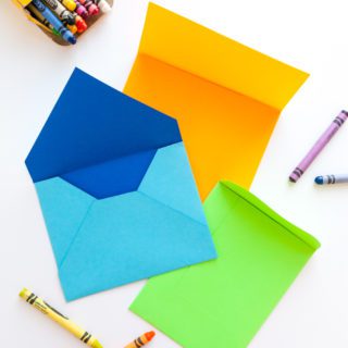 A blue, green and orange handmade envelope surrounded by crayons.