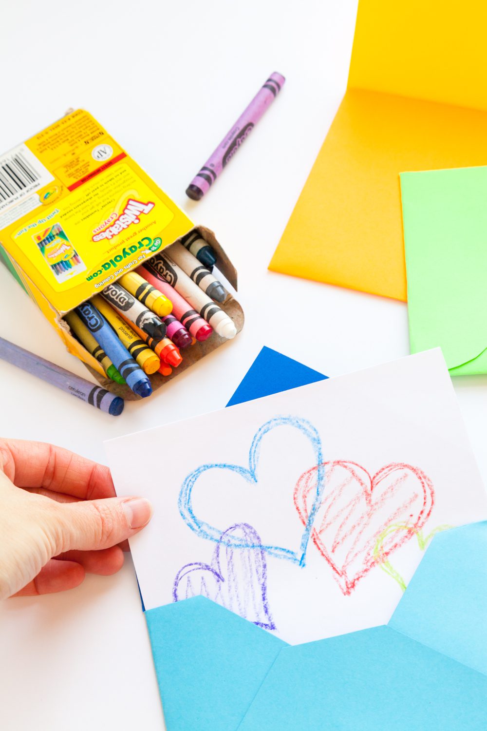 Pulling a card with hearts from a blue handmade envelope, with crayons and colorful paper nearby.