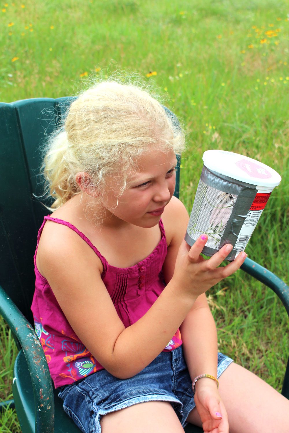 A young girl looks at the bug box she has made from a yogurt container.