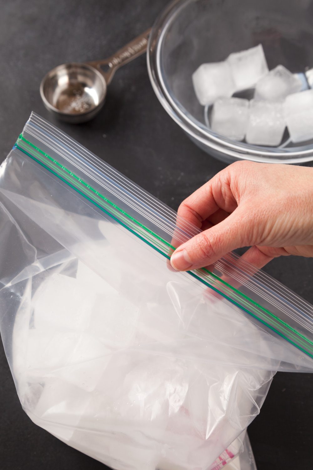 A hand closing up a ziploc bag of ice with salt making ice cream with milk.