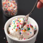 A spoon taking a bite of homemade ice cream in a bowl with sprinkles on top.
