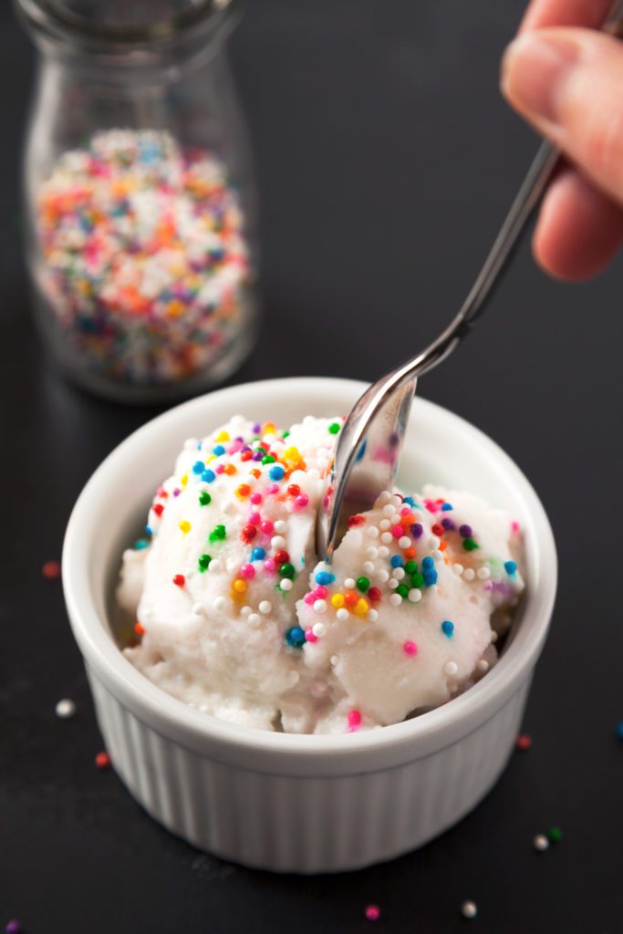 A spoon taking a bite of homemade ice cream in a bowl with sprinkles on top.