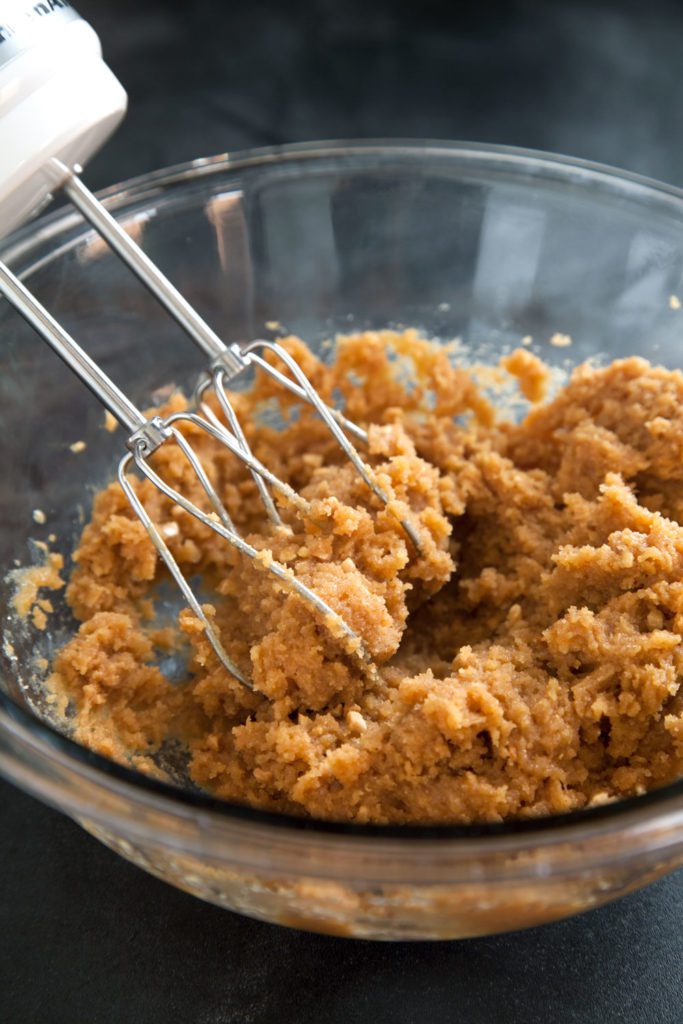 Hand mixer beating peanut butter cookie dough in a mixing bowl.