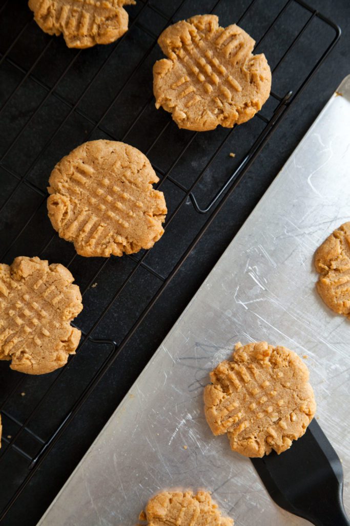 Peanut butter cookies on a baking sheet, and cookies on a cooling rack.