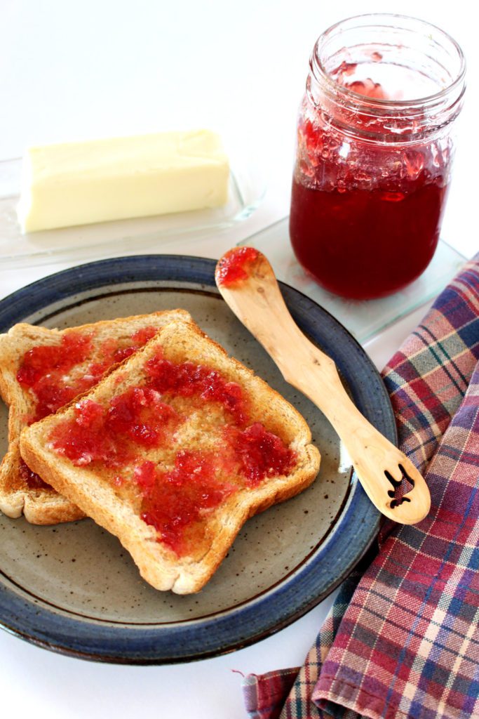 Toast spread with fruit jelly on a plate with butter and a jelly jar in the background.