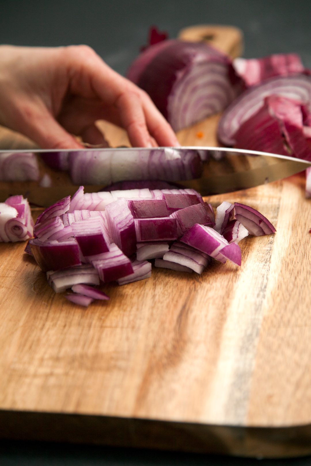 A knife cutting red onions on a cutting board.