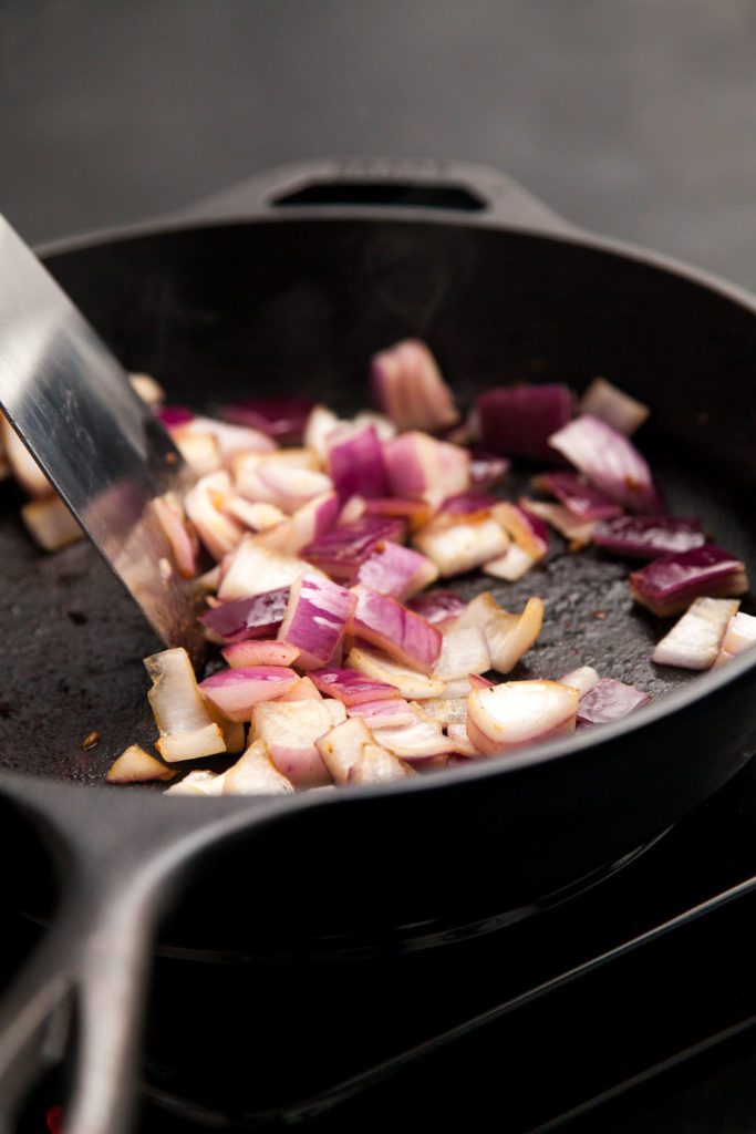 Red onions being sautéed in a cast iron skillet.