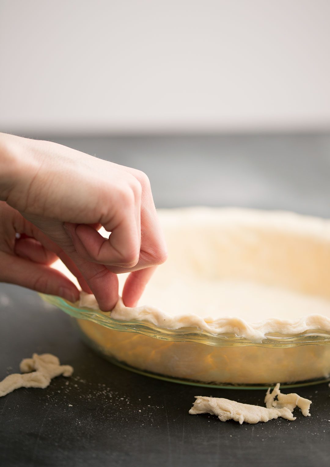 Hands scalloping the edges of an unbaked pie crust.