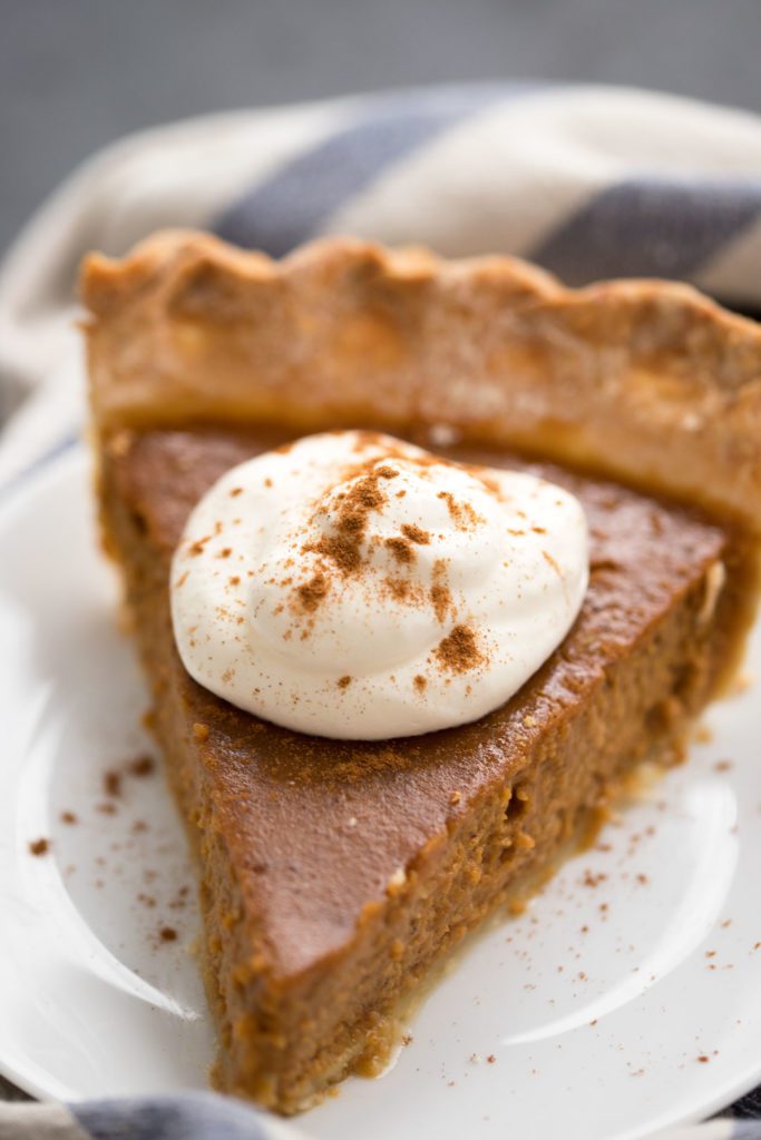 A single serving of pumpkin pie topped with whipped cream and cinnamon.