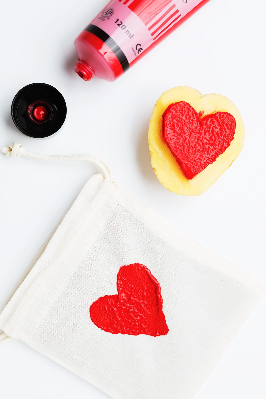 Red paint tube, a potato cut into a heart stamp, a drawstring bag with a red heart stamp.