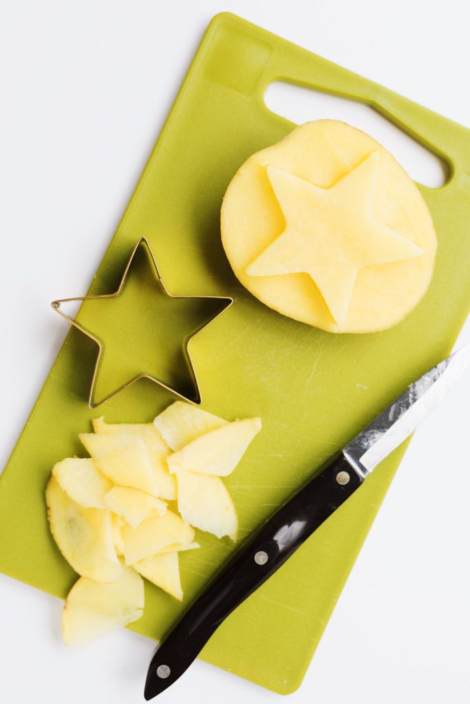 A cutting board, paring knife, star cookie cutter, and a potato cut into a star stamp.