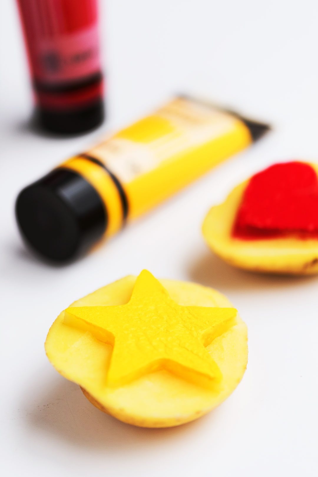 Red paint tube, yellow paint tube, and two potato halves with a hart and star stamp cut into them.