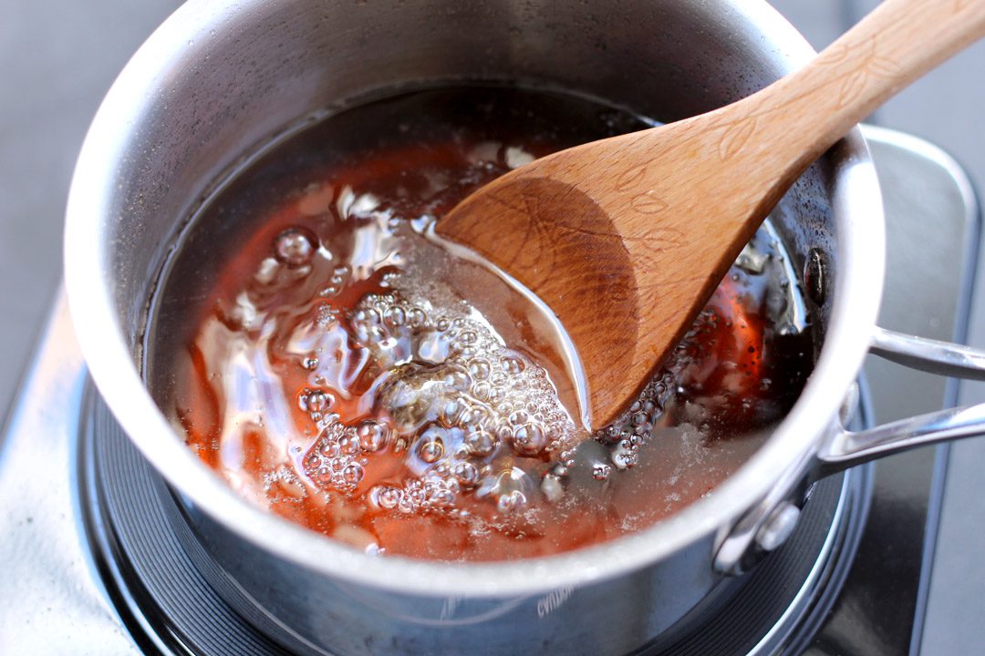 A wooden spoon stirring a pot of simmering homemade pancake syrup.