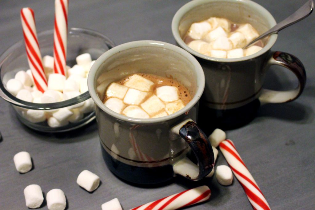 Hot chocolate in mugs with marshmallows and candy canes.