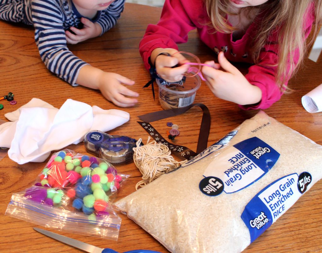 Children playing with a rubber band, pom poms, rice, and ribbon.