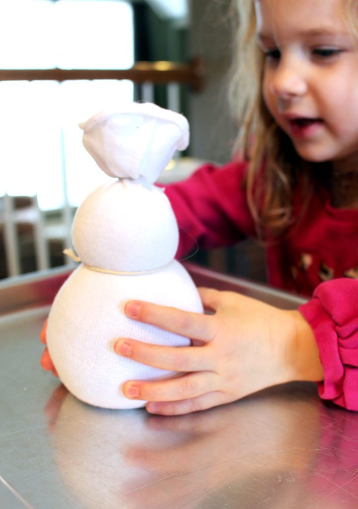 Child holding a sock filled with rice, shaped into a snowman.