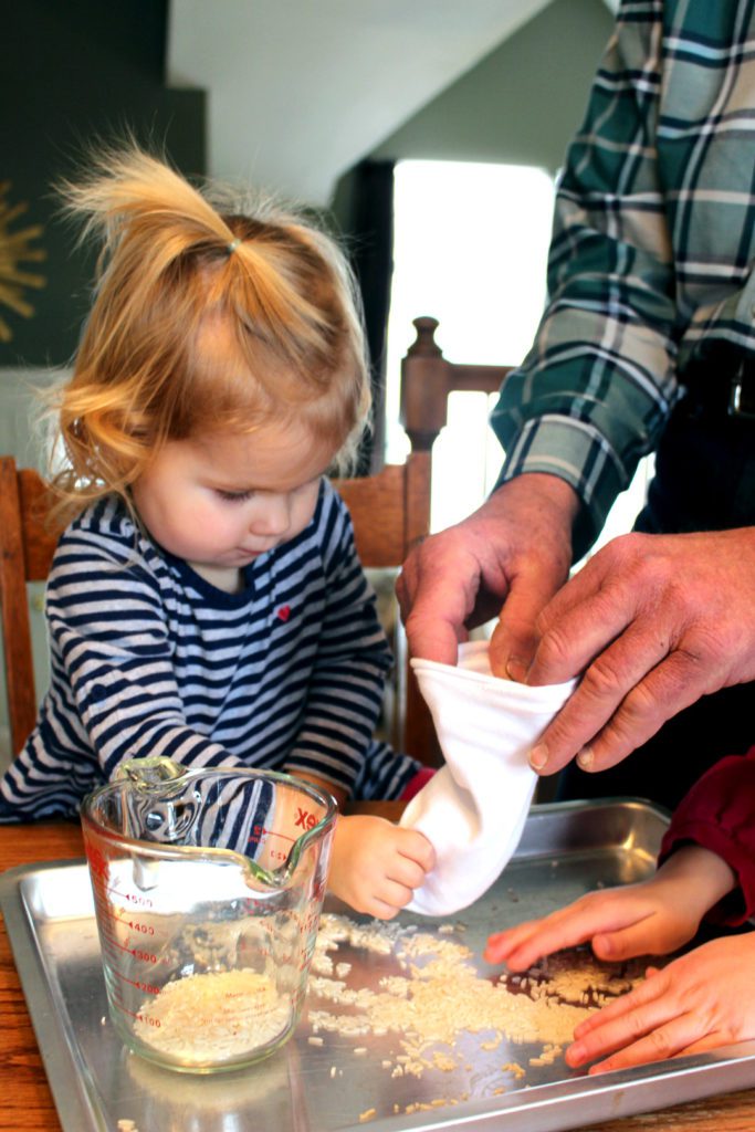 Child and adult filling a sock with rice over a pan.