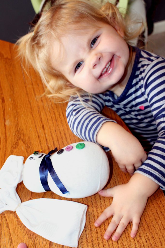 Child smiling with a sock snowman.