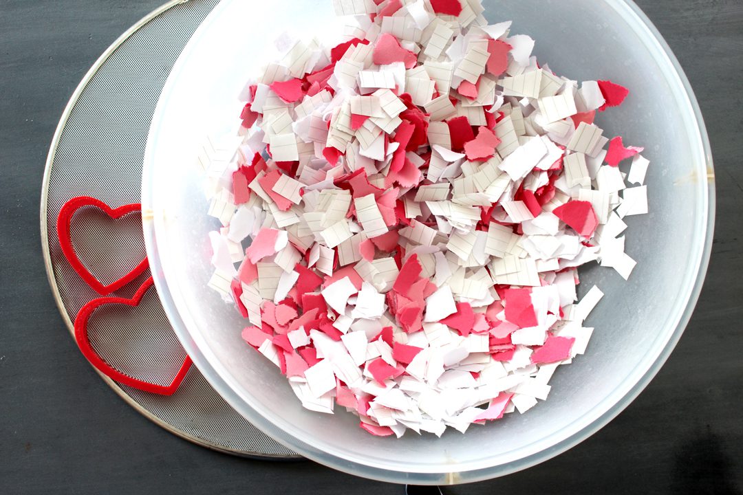 A bowl with red and white paper scraps, two heart cookie cutters, a splatter screen.