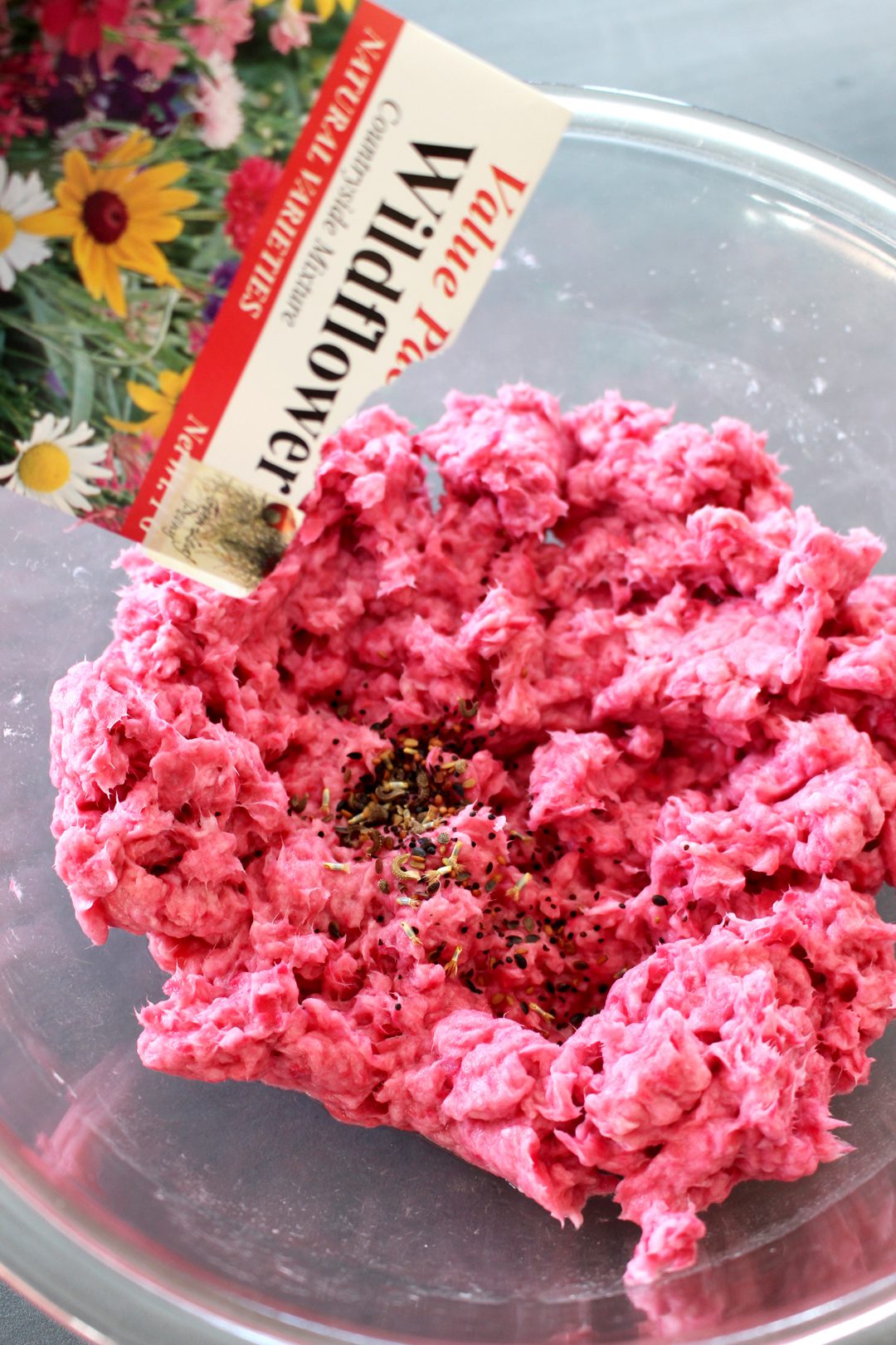 Pouring wildflower seeds into pink paper pulp in a bowl.