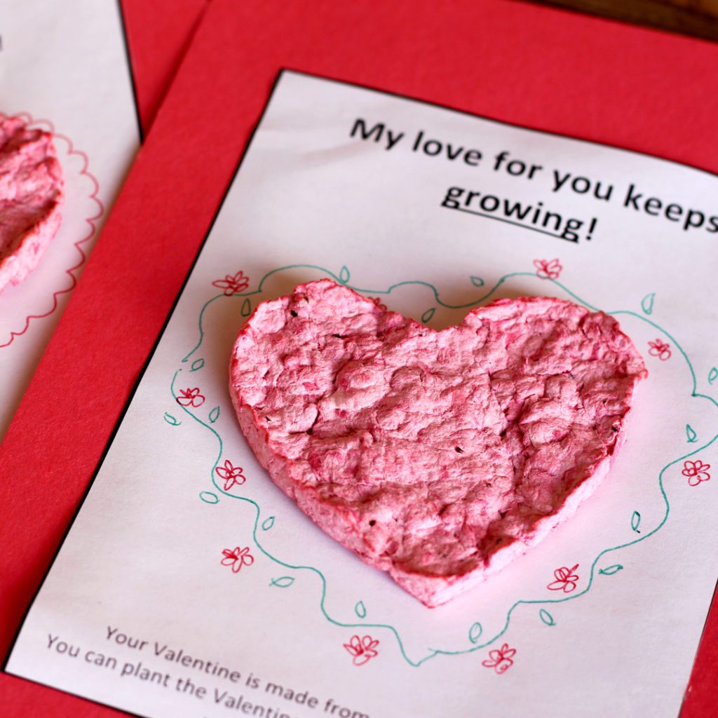 A pink paper heart valentine on a decorated card.