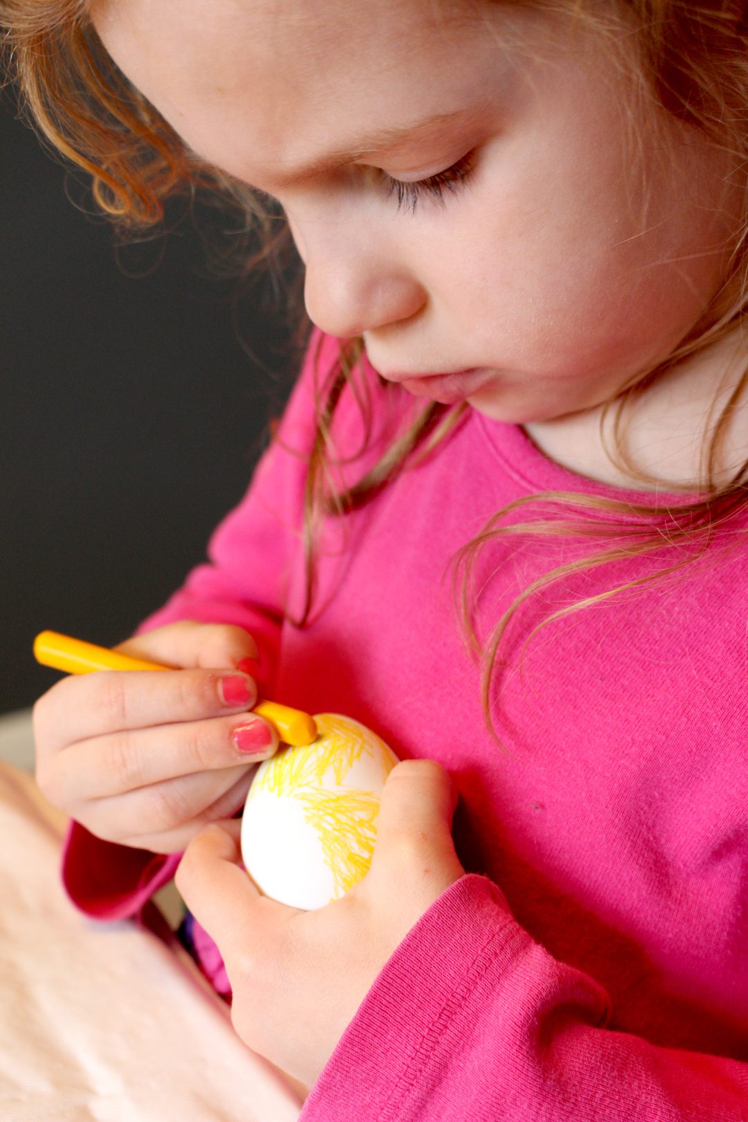 A child coloring an easter egg with a yellow crayon.