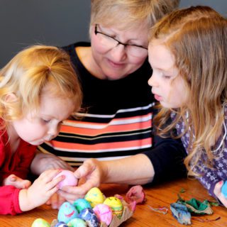 Kids and their grandma looking at colorful decorated Easter Eggs.