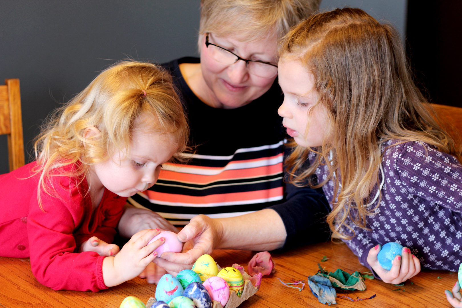 Kids and their grandma looking at colorful decorated Easter Eggs.