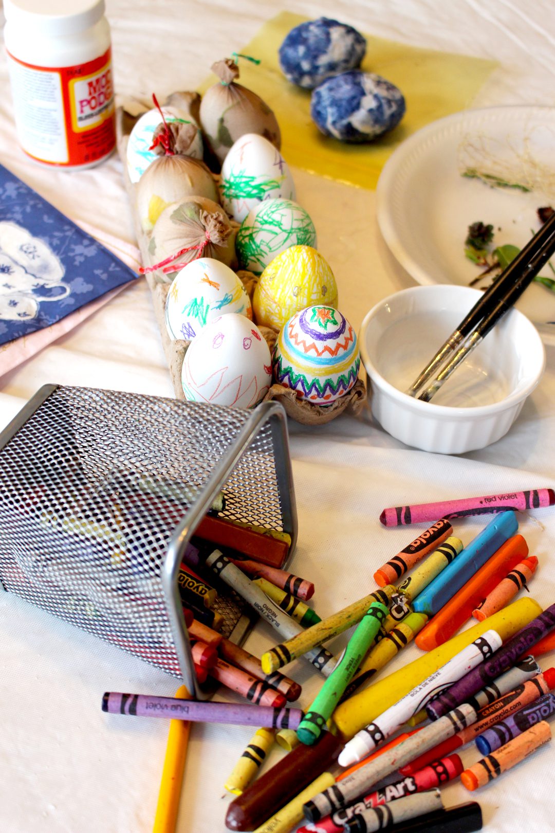 Colored Easter eggs surrounded by Mod Podge, paint brushes, and crayons.
