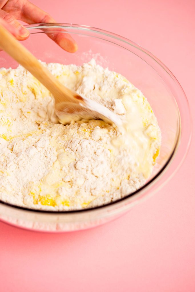 A bowl of flour and ingredients being mixed into a batter with a wooden spoon.