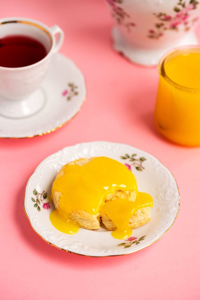 A scone topped with lemon curd on a decorative plate.