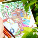 A hand holding colored pencils and a month of June coloring page with a tree house in a large tree.