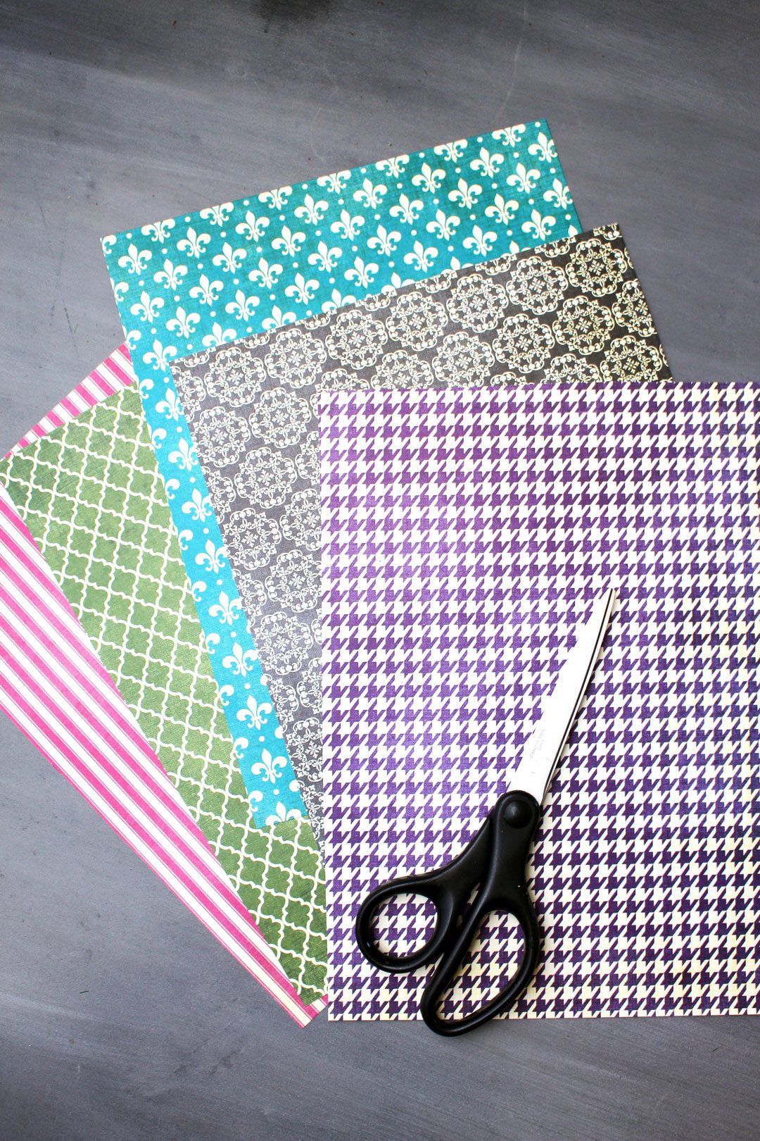 Pink, green, teal, black, and purple patterned pieces of scrapbook paper and a pair of scissors.