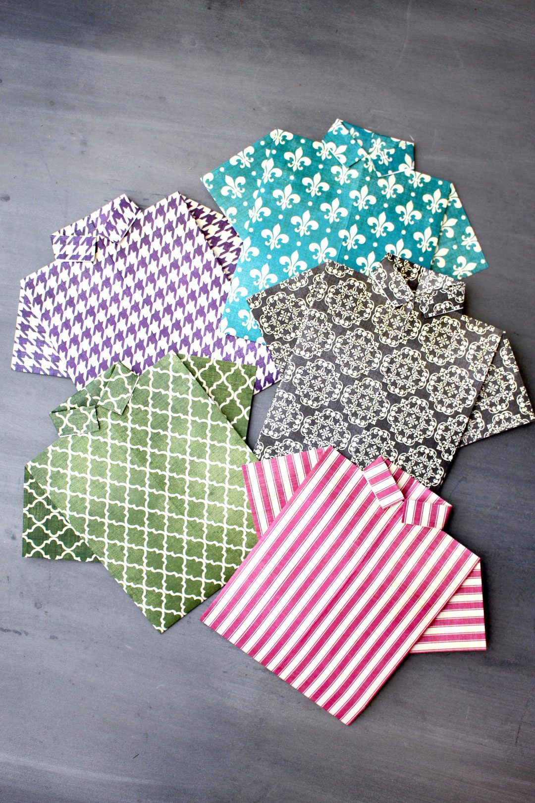Pink, green, teal, black, and purple patterned pieces of scrapbook paper folded into origami shirts.