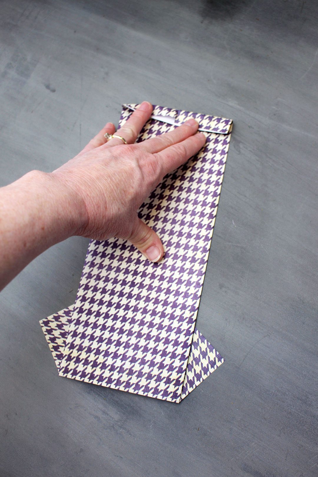 A hand folding a purple houndstooth pattern folded origami shirt.
