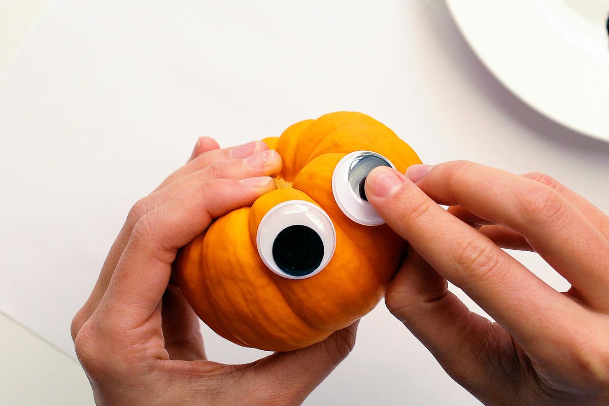 Adding googly eyes to a mini pumpkin craft.