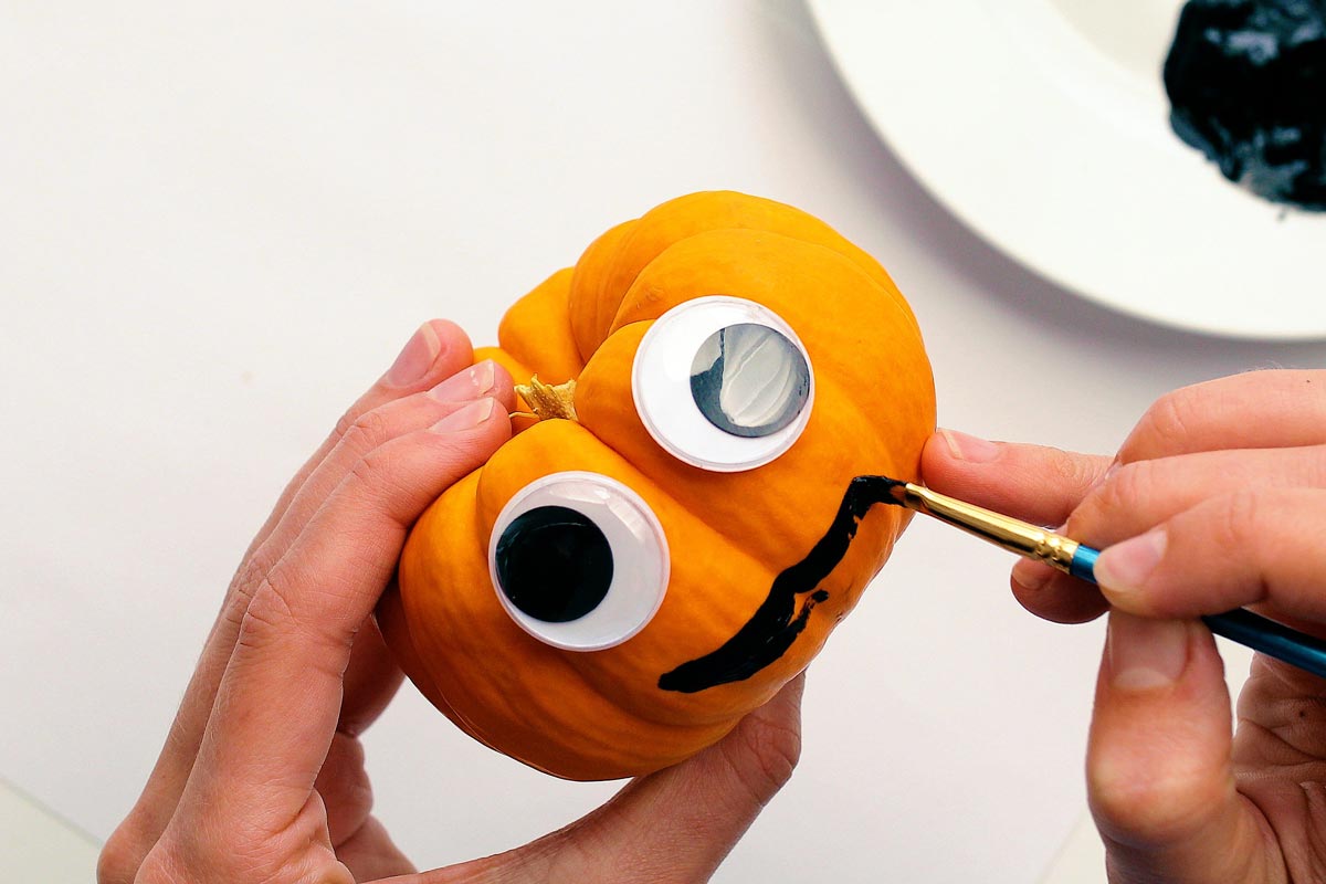 Painting a smile on a mini pumpkin with googly eyes as a craft.