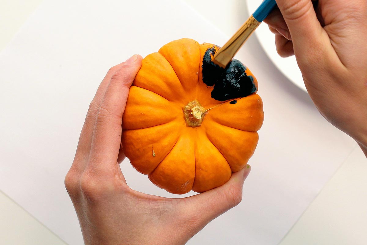 A paintbrush painting a mini pumpkin black.