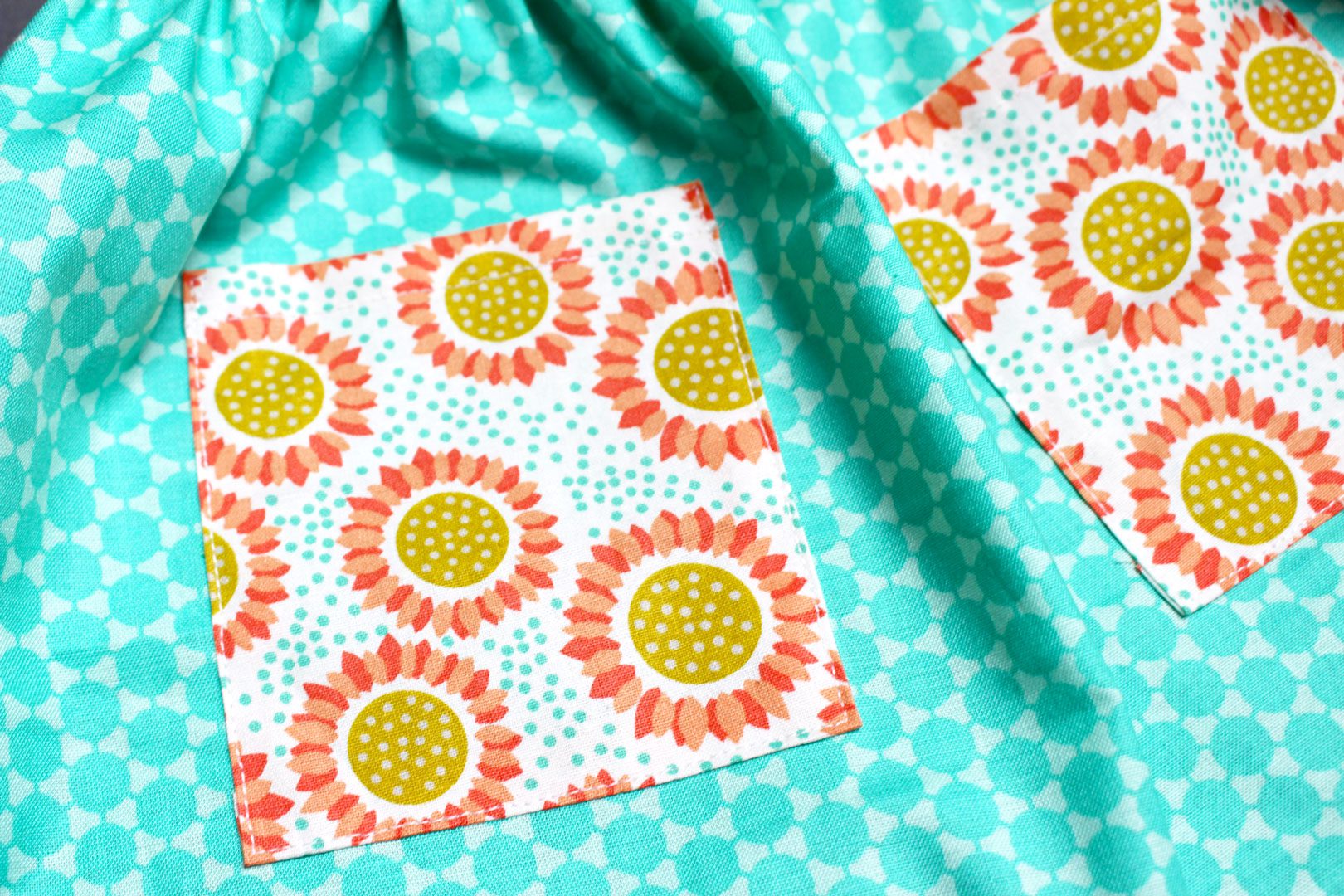 Orange floral pocket fabric squares sitting on the teal fabric of an apron after sewing.