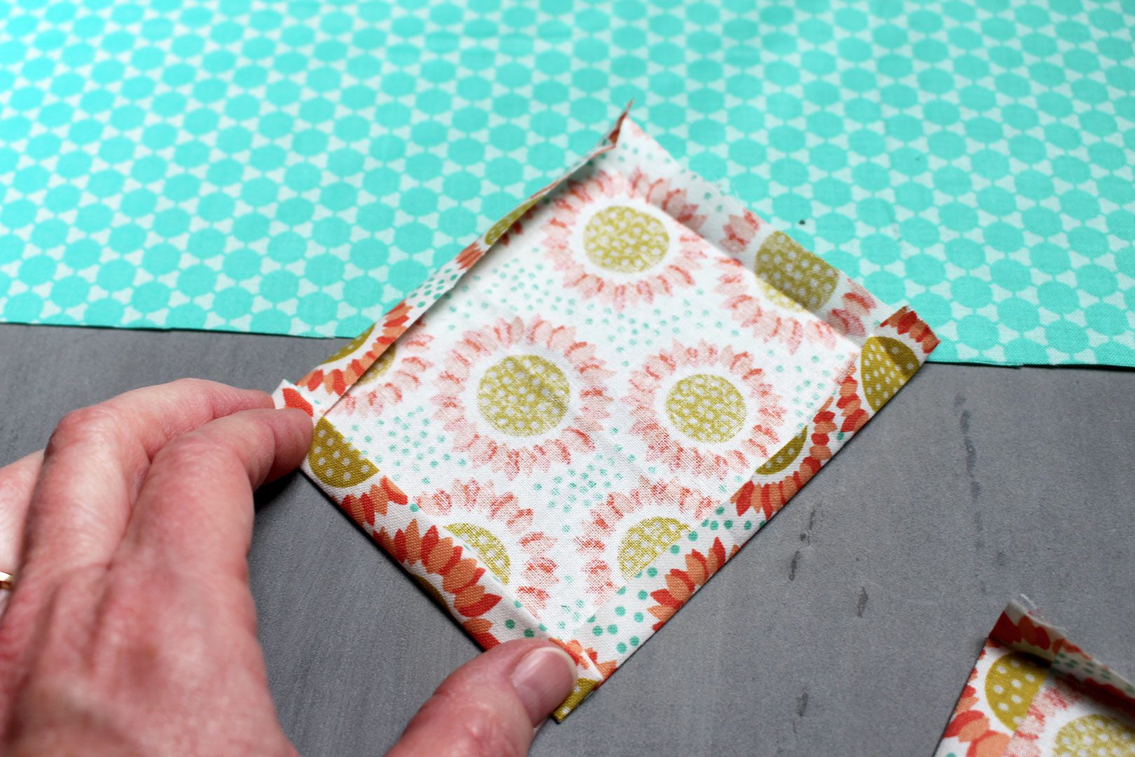 The edges of an orange floral square of fabric ironed over before sewing.