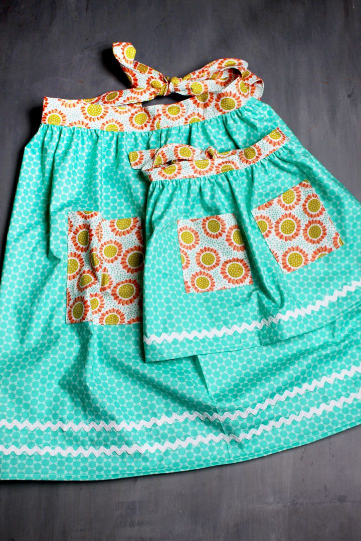 A miniature and a full sized teal and orange flowered DIY Apron.