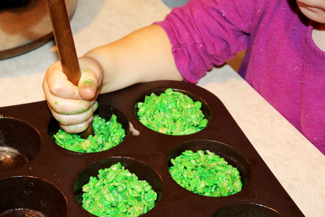 A girl pressing a hole into the center of holiday wreath cookies with the handle of a wooden spoon.