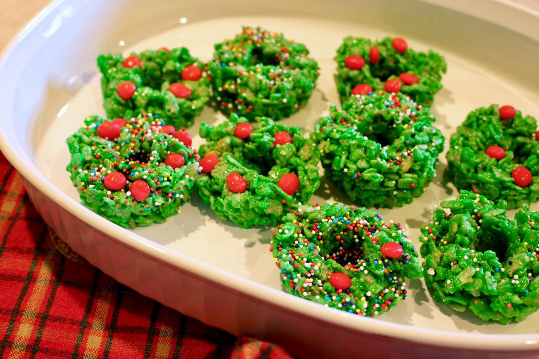 A platter of green Christmas Wreath Cookies decorated with sprinkles and red hot candies.