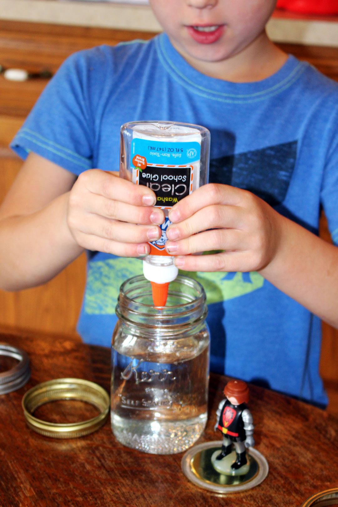 Child adding clear glue to a mason jar with water.