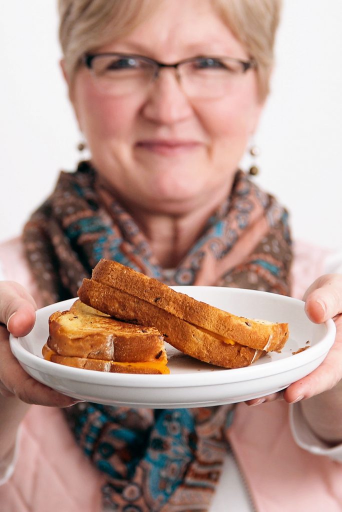 A woman holding out a plate of grilled cheese sandwiches.
